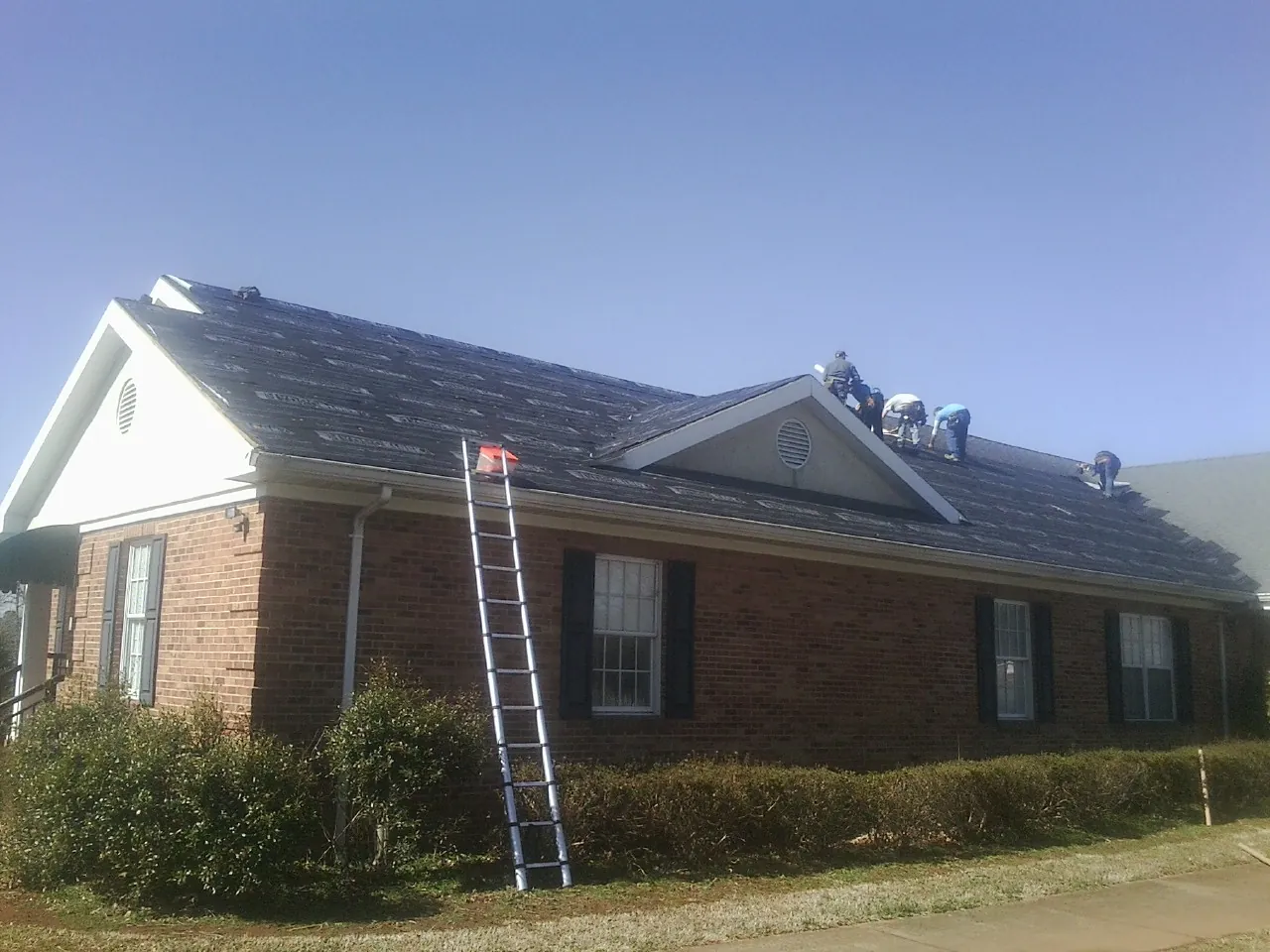 Crew tearing shingles off a brick ranch roof with a ladder set — Emergency Roof Repair work by our crew in Harwich