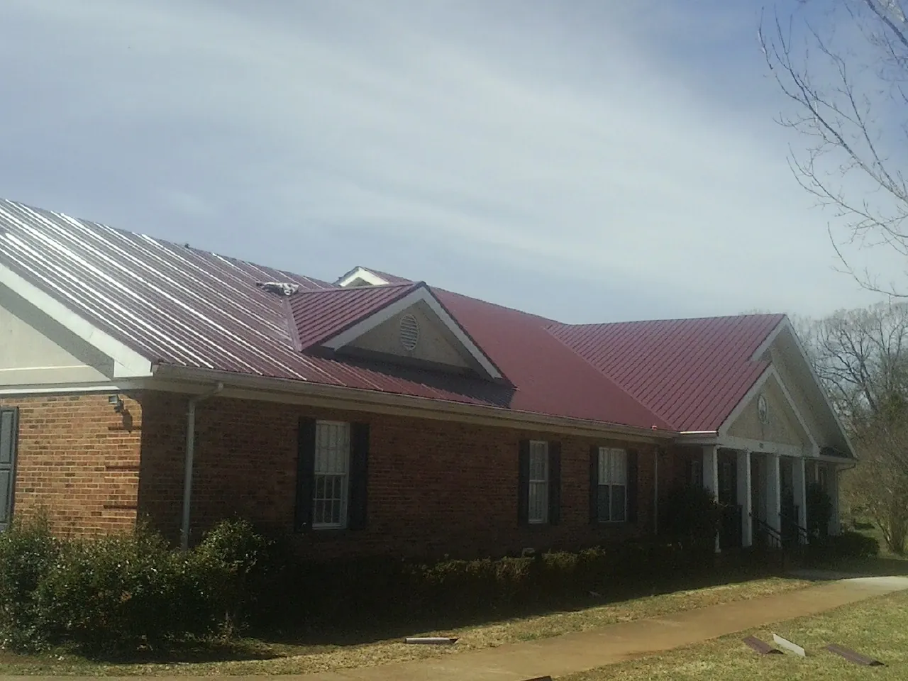 Red metal roof with gabled entries on a long brick building, from a Hail Damage Roof Repair job in Harwich