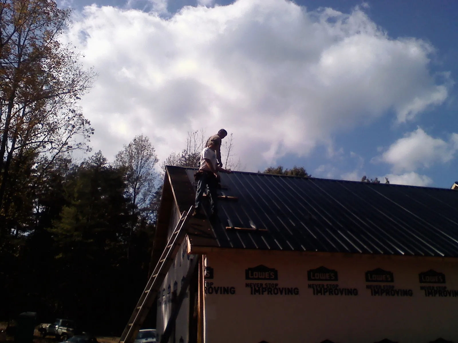 Roofer fastening dark metal panels high against a cloudy sky, from a Roof Inspection job in Harwich