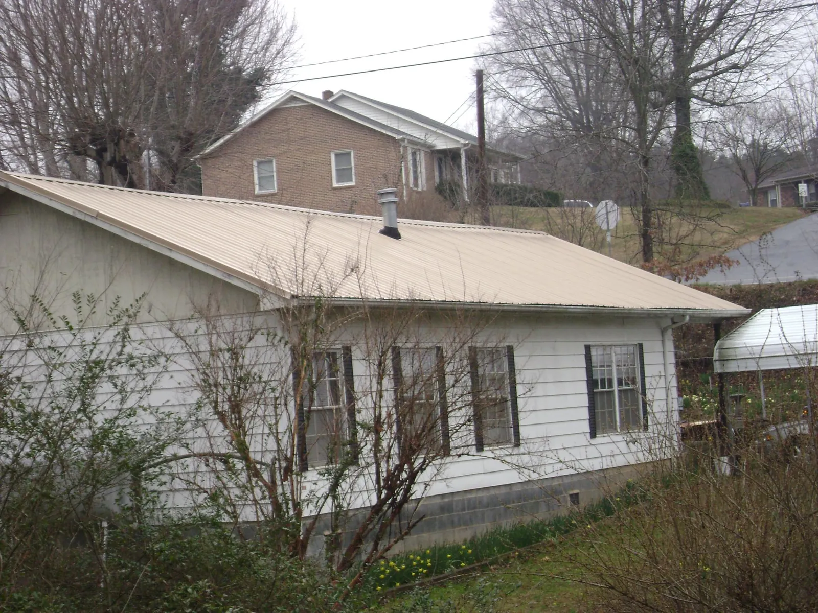 Tan metal roof on a white sided house set into a hillside — Commercial Roofing by Roofing Brothers in Harwich